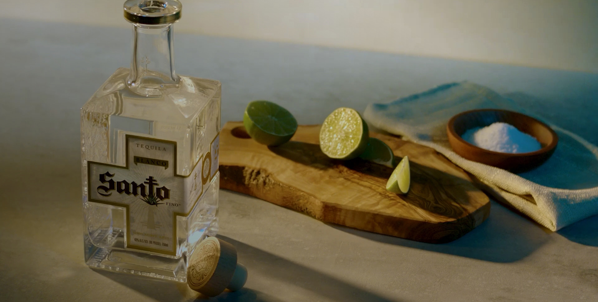 Bottle of Santo Tequila next to a cutting board with cut limes and a wooden dish of salt.