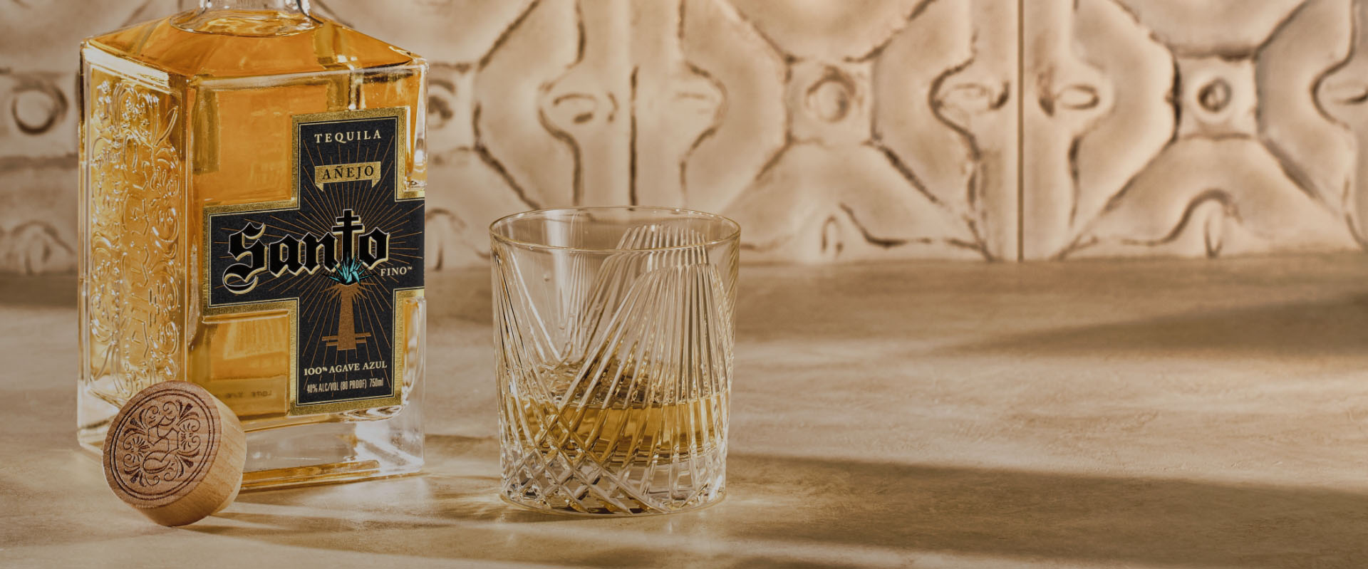 Bottle of Santo Añejo sitting on counter next to cork and glass tumbler.