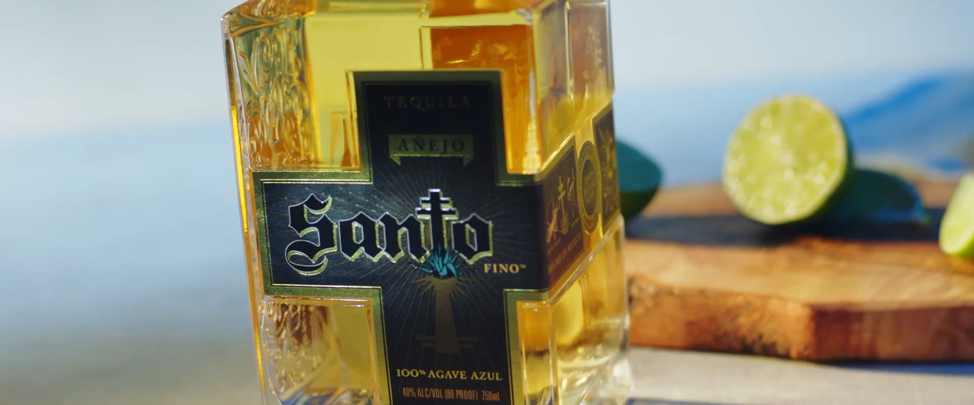 Bottle of Santo Añejo tequila with cut limes sitting on a cutting board in the background.