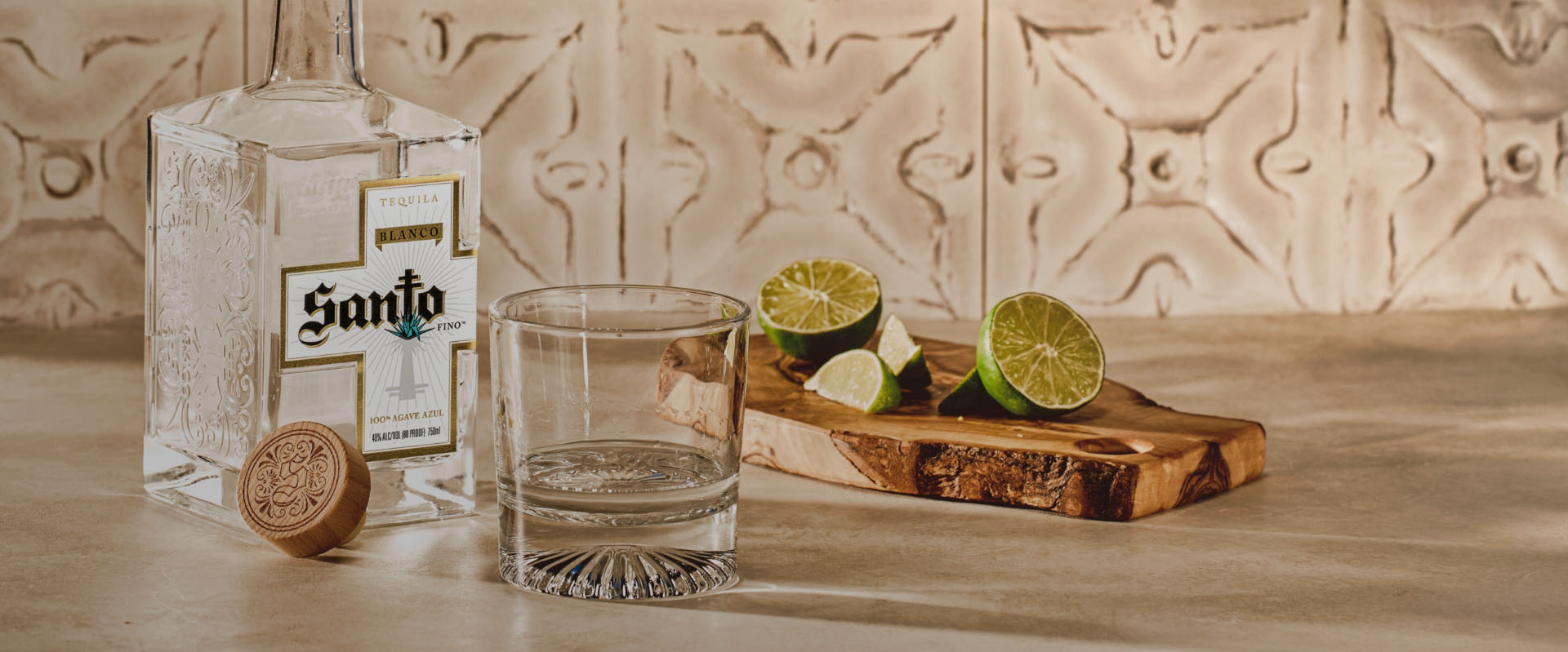 A bottle of Santo Blanco tequila on counter next to cut limes on a cutting board and a glass tumbler.