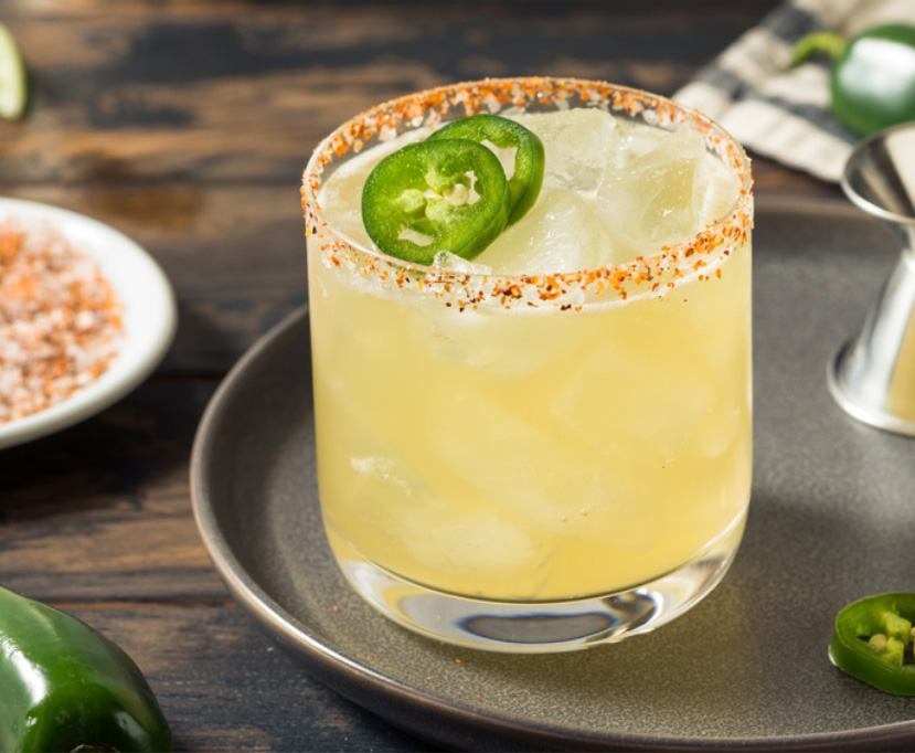 Glass tumbler on a tray filled with an easy spicy margarita recipe, ice, chili pepper and salt rim, and jalapeño slices for garnish.