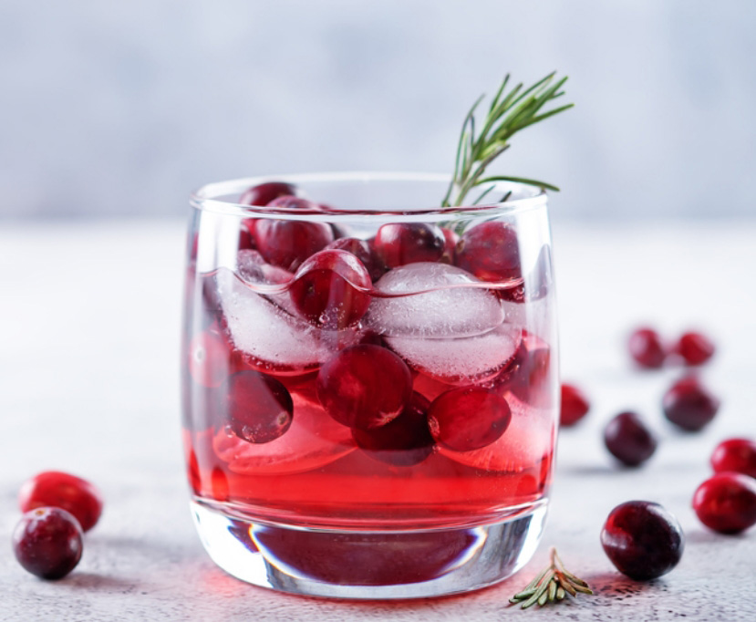 Glass tumbler filled with a cranberry margarita recipe, ice, and cranberries and rosemary sprig garnish.