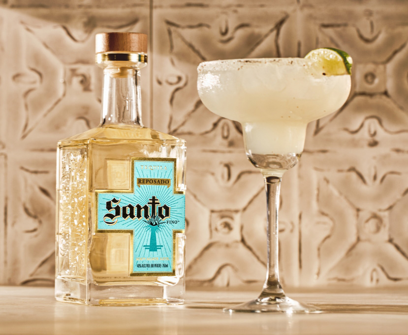 Margarita glass filled with a ginger margarita recipe and lime wedge next to a bottle of Santo Tequla.