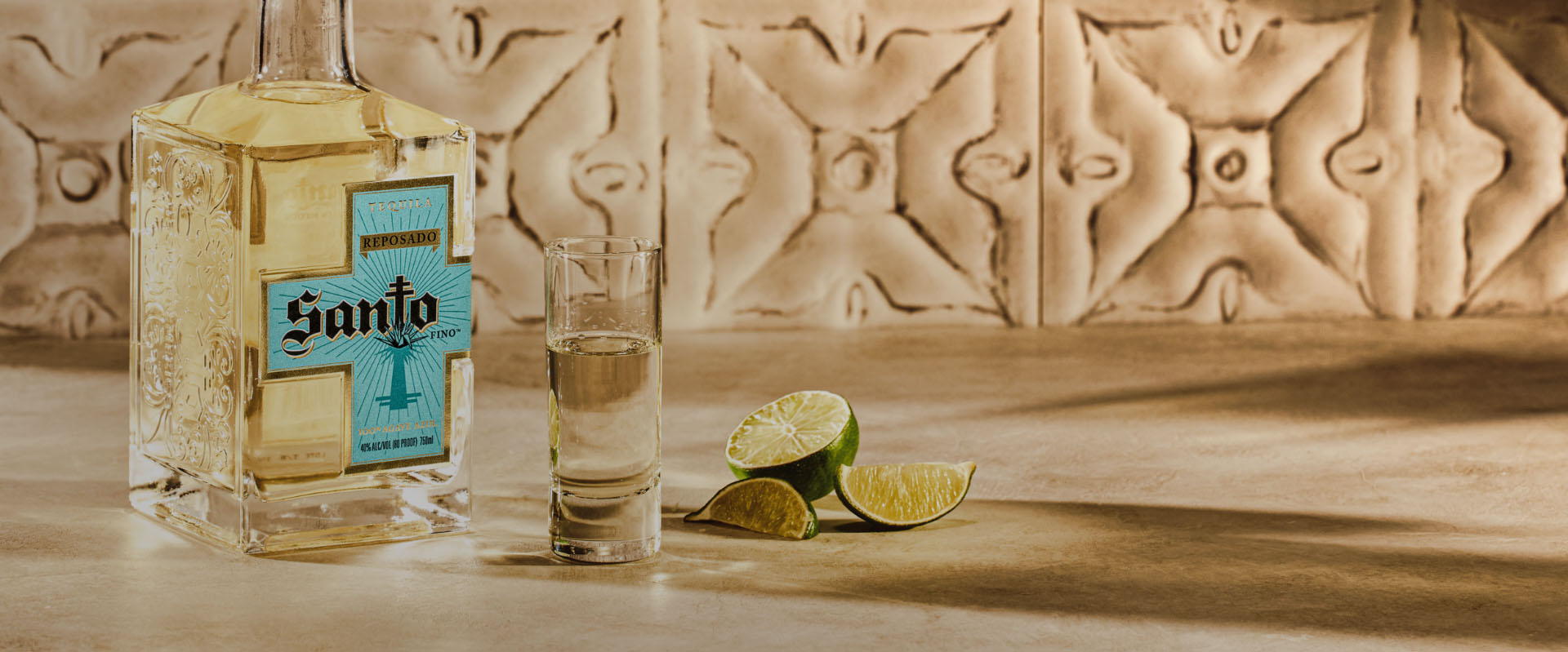 Bottle of Santo Reposado on counter next to cut limes and a shot glass.