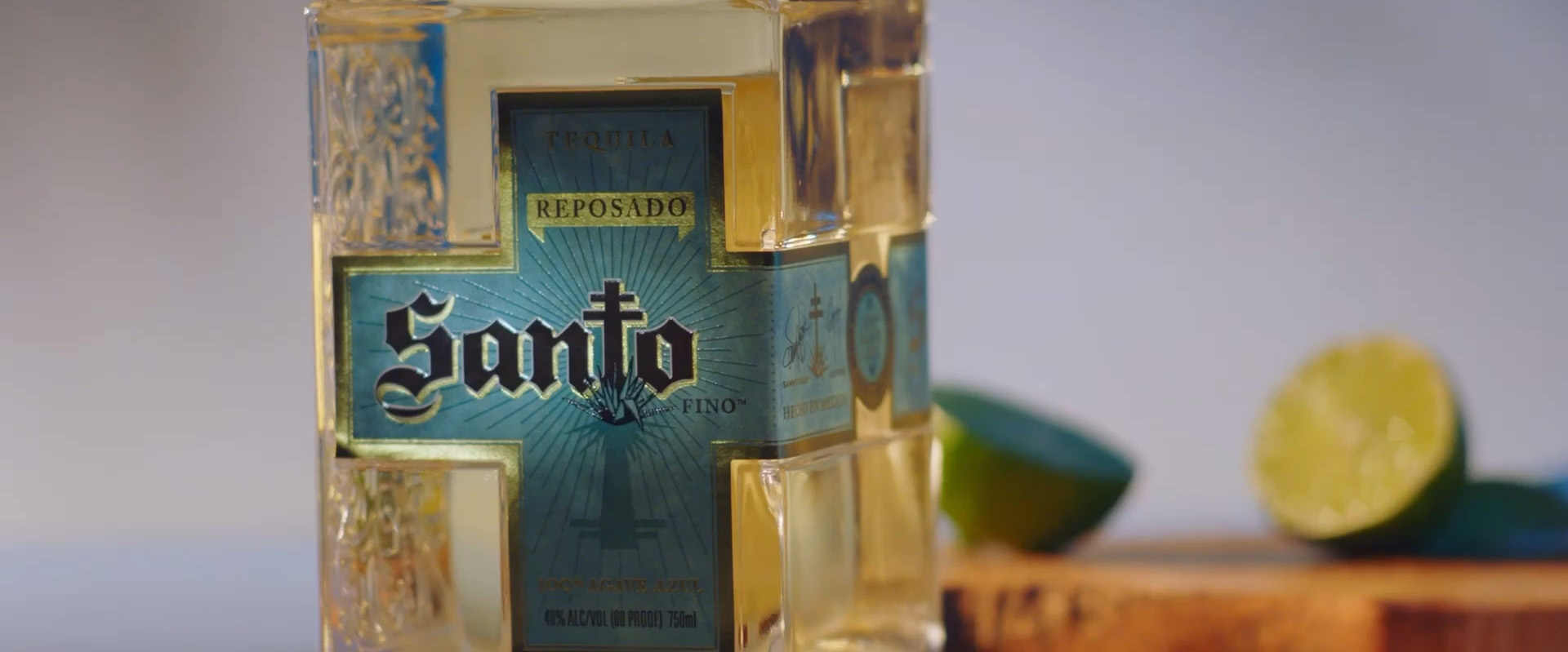 Bottle of Santo Reposado tequila with cut limes on cutting board in the background.